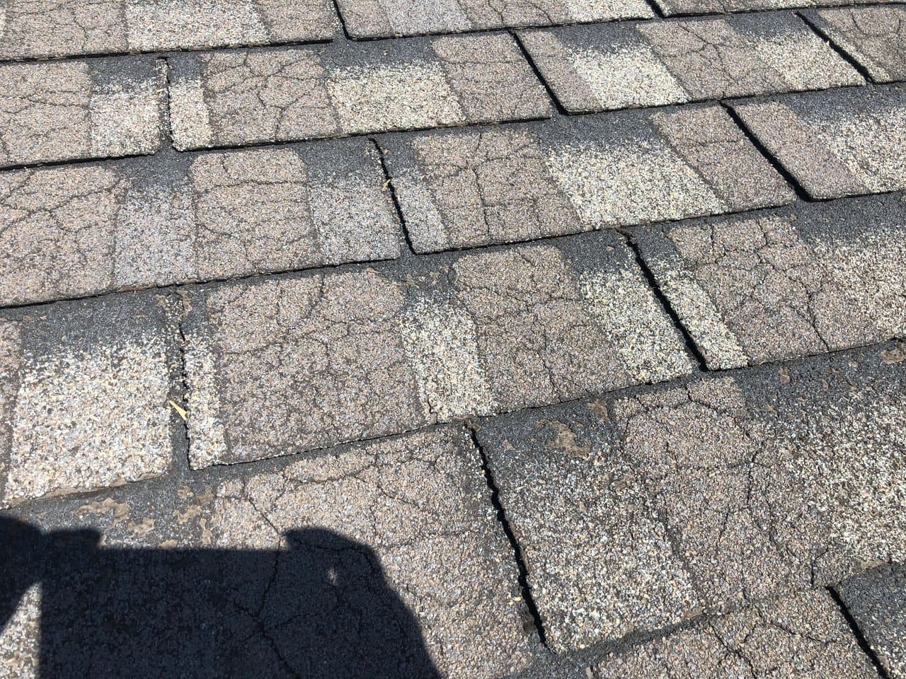 Close view of aging asphalt shingles with cracks and worn, patchy granules