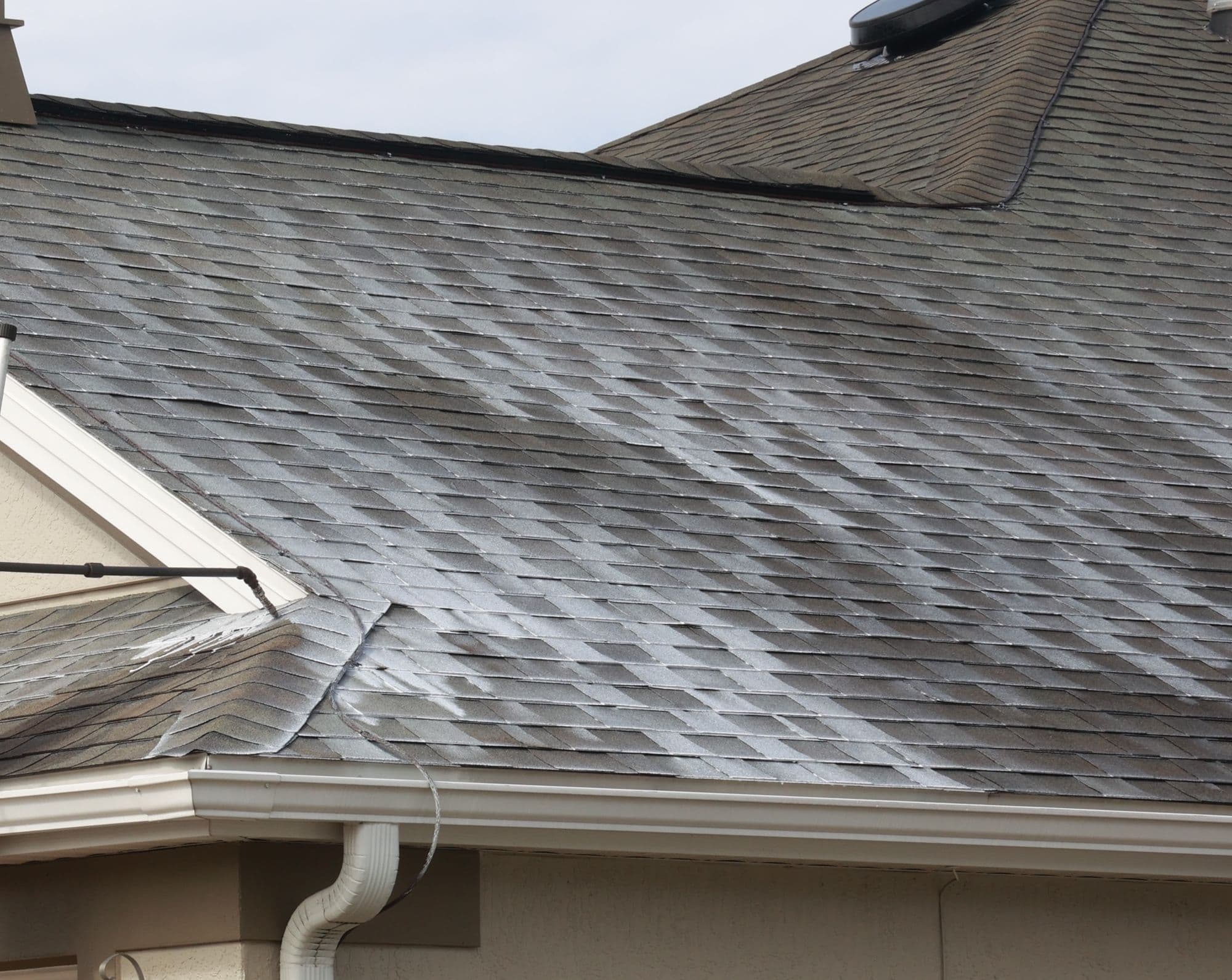 Asphalt-shingle roof partway through treatment: treated shingles darker and deeper in color beside dry, faded ones